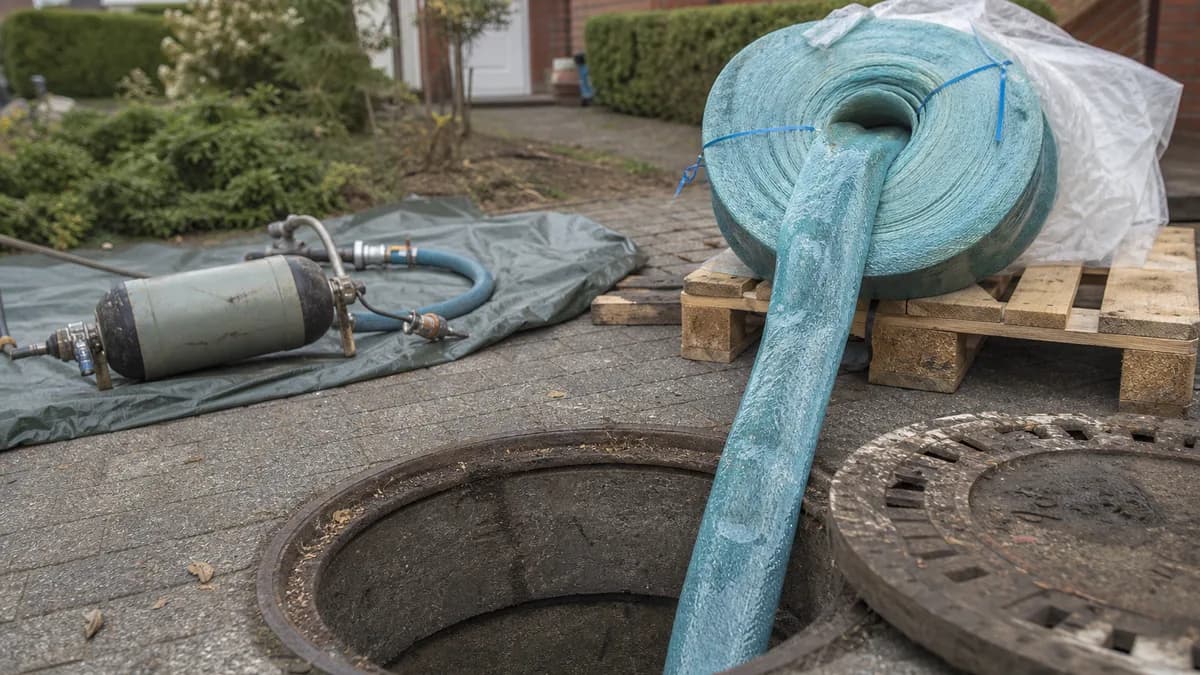 Fachkraft zieht über einen offenen Revisionsschacht auf einem Wohngrundstück einen harzgetränkten Schlauchliner in eine Abwasserleitung ein